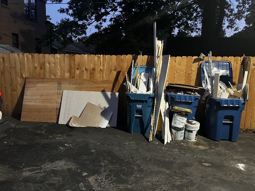 Plywood, drywall, buckets and overflowing bins piled against a wooden fence before removal